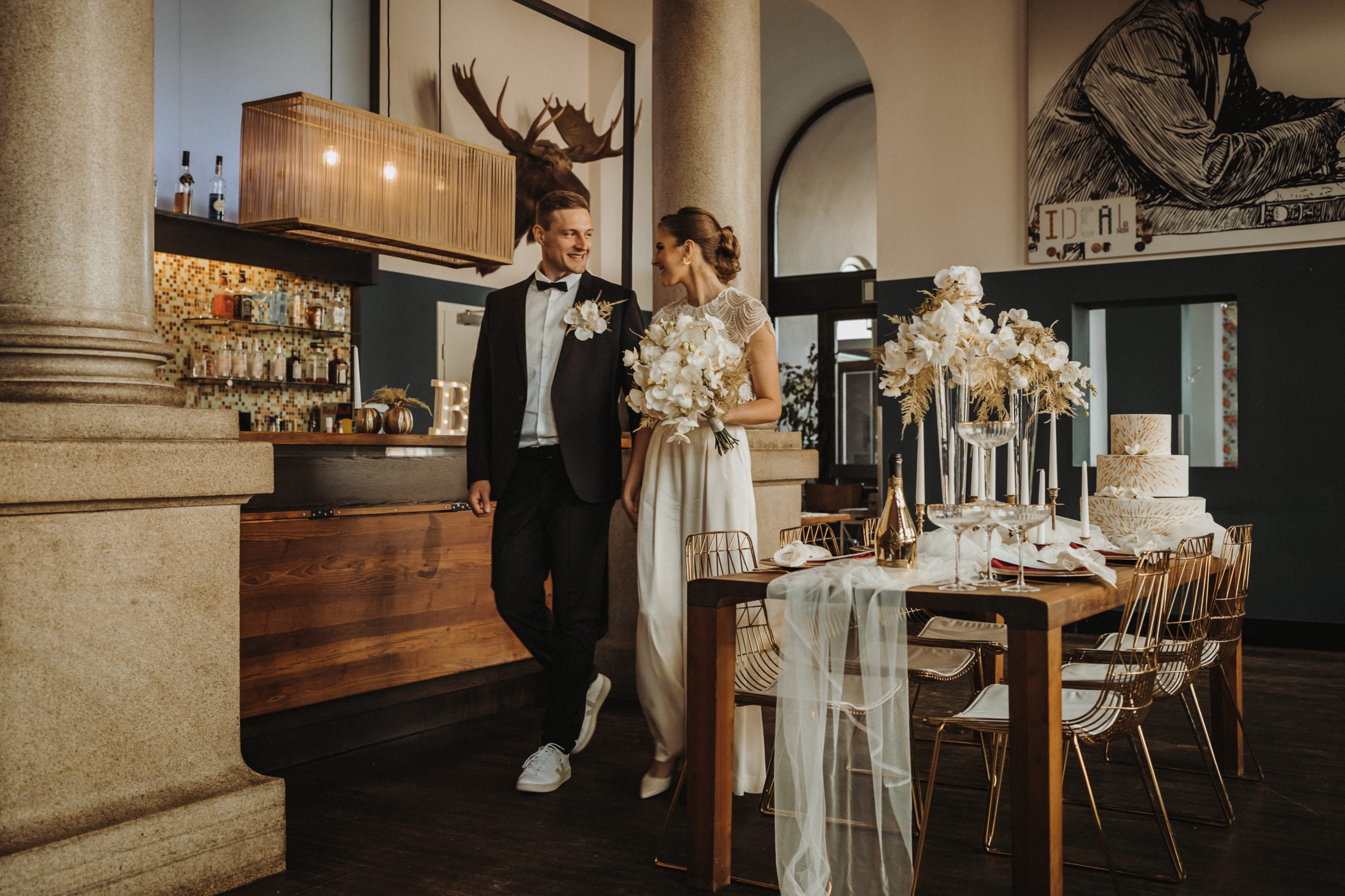 Brautpaar an der Bar des IDEAL, umgeben von weißen Orchideen und der IDEAL-Wandmalerei